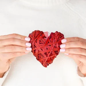 lipoprotein a: A person holding a woven red heart in front of a white sweater, symbolizing heart health awareness.