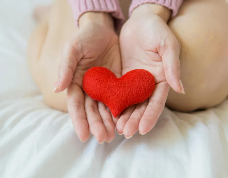 Hormone Therapy: Hands cradling a red fabric heart against a white background.