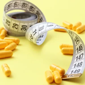 Yellow capsules and a measuring tape on a yellow background, symbolizing Vitamin D and Weight Management.