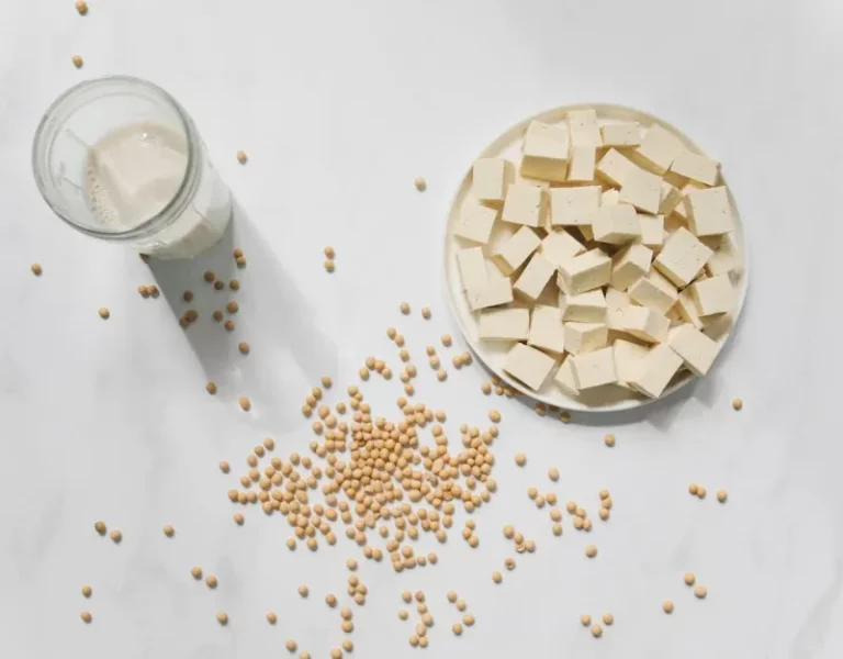Tofu cubes, soybeans, and a glass of soy milk arranged on a white background