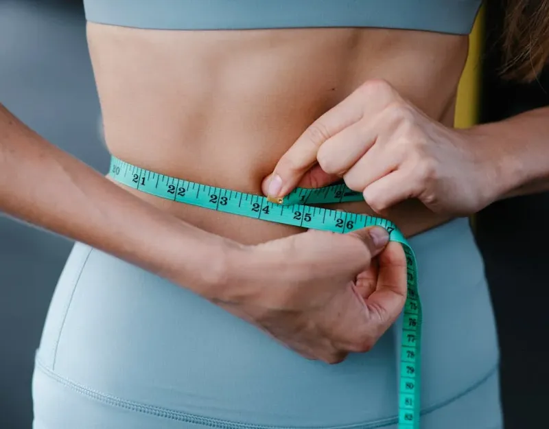 Zenith Supplement: Person measuring their waist with a tape measure while wearing workout clothes